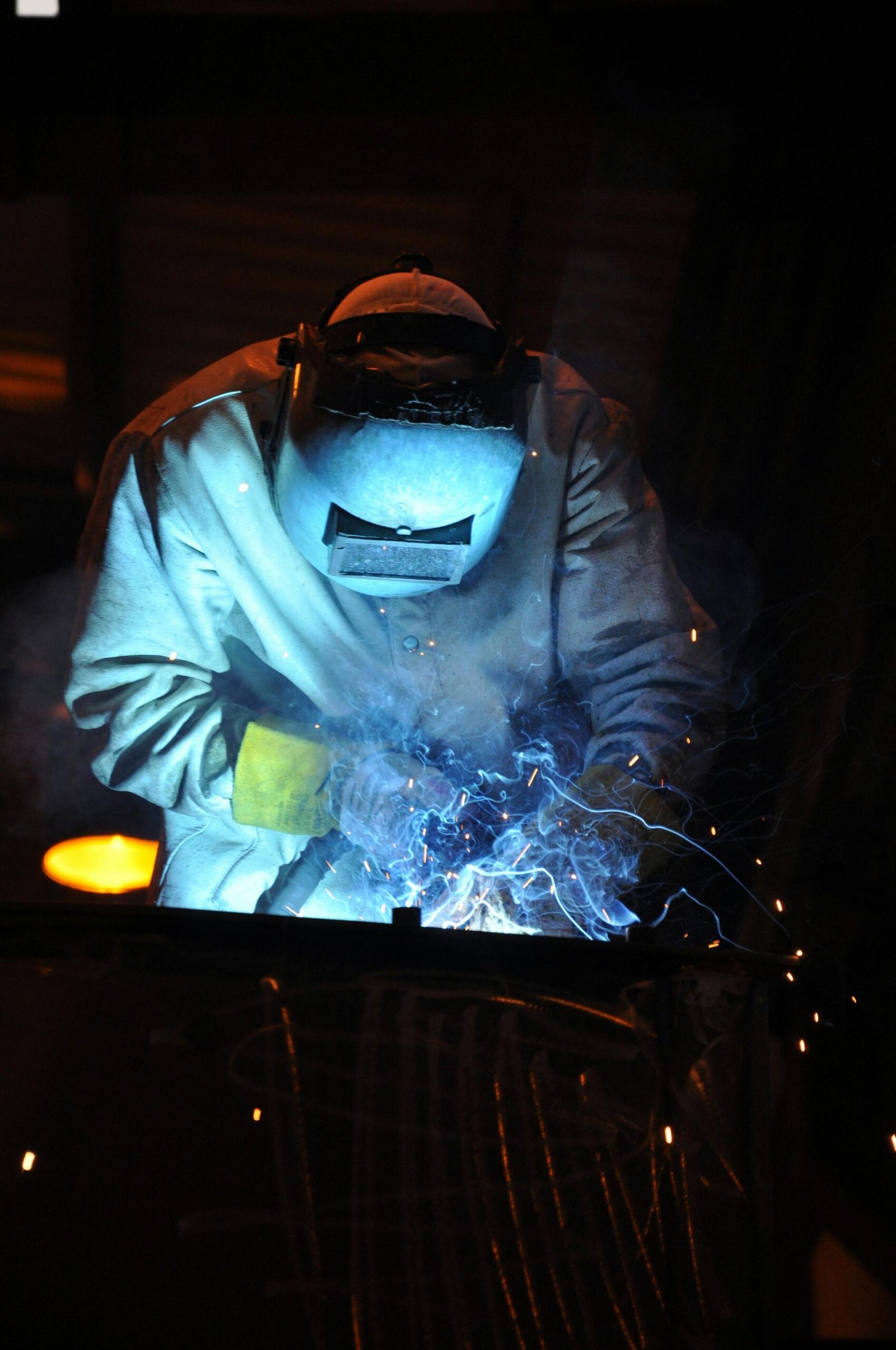 A skilled welder working in a dark workshop with blue sparks flying, showcasing metalworking expertise.