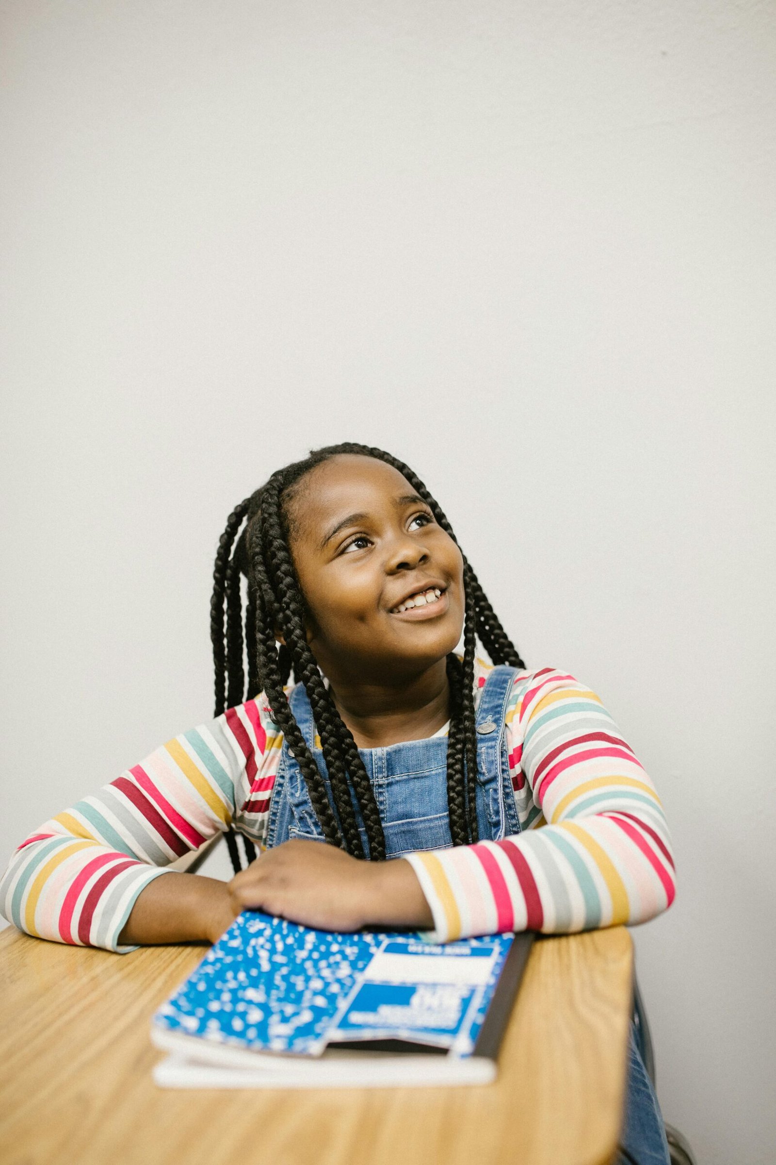 A cheerful young black girl smiling while sitting at a desk with a notebook in classroom.